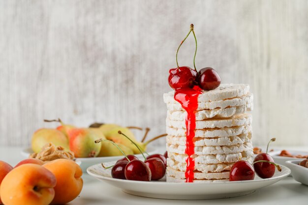 Rice cakes in a plate with cherry, nuts, pears, apricots, peanut butter