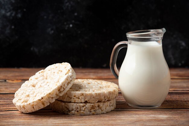 Rice crackers and glass jug of milk on wooden table. 