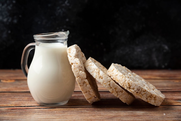 Rice crackers and glass jug of milk on wooden table. 