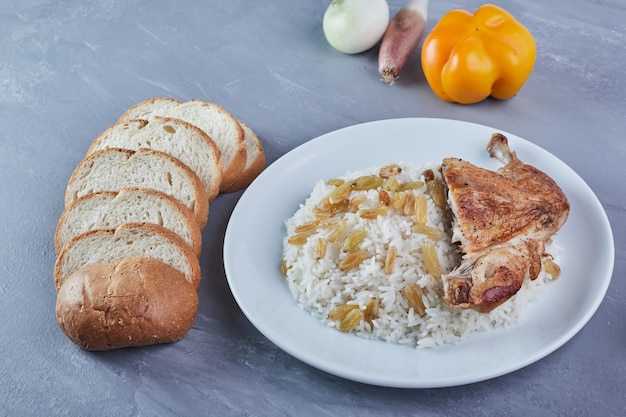 Rice garnish with sultana and fried chicken in a white plate with bread.