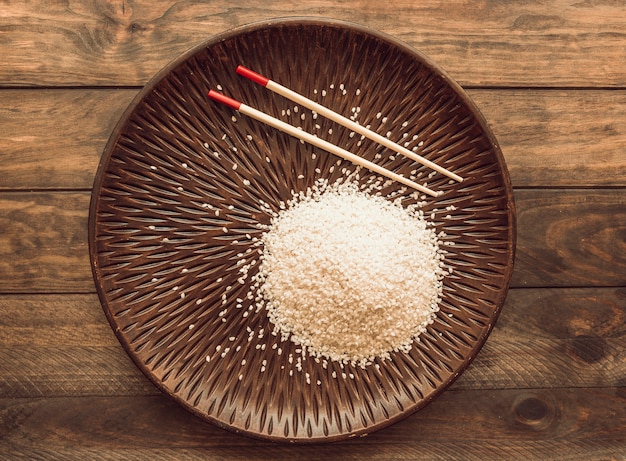 Rice grains on wooden plate with chopsticks over the wooden background