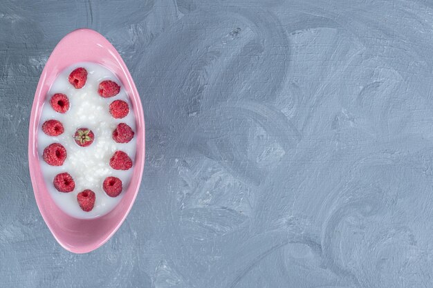 Rice pudding in a pink bowl topped with raspberries on marble table.