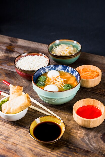 Rice; spring rolls; sauces; beans sprout; grated carrots with fish ball soup on desk against black background