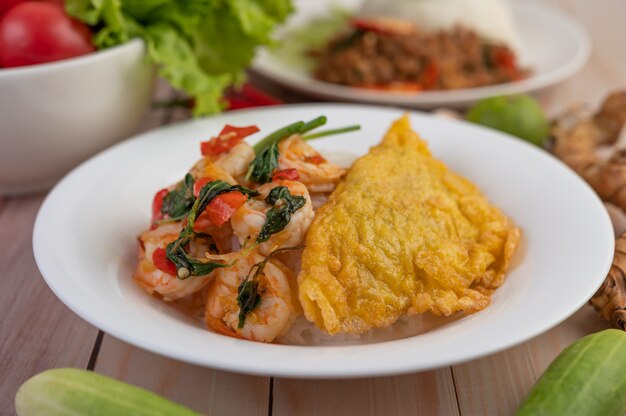 Rice topped with shrimp and omelet on a white plate.