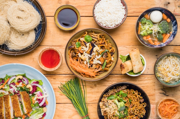 Rice; udon noodles; spring rolls; chives; sprout beans; fish ball soup and salad on table