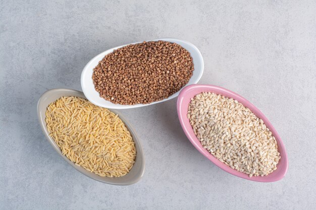 Rice, wheat and buckwheat in bowls on marble.