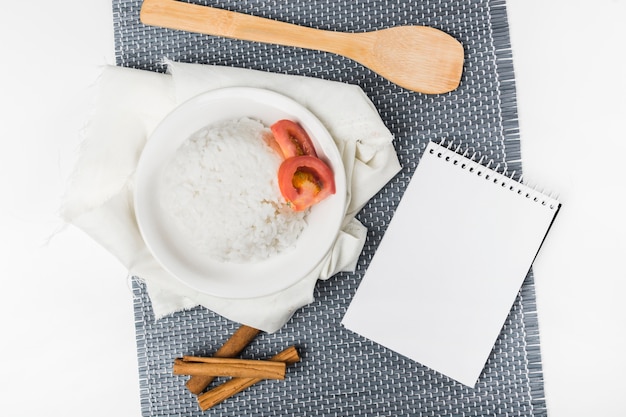 Рис с томатным ломтиком и палочками корицы с лопаточкой и блокнотом на столешнице
