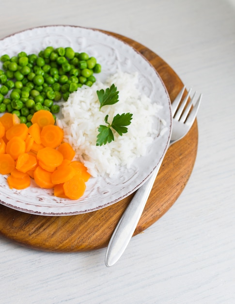 Рис с овощами и петрушкой на тарелке на деревянной доске