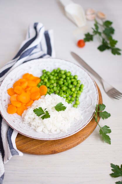 Rice with vegetables and parsley on wooden board near napkin and fork