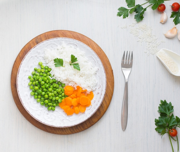 Rice with vegetables on wooden board near fork and garlic