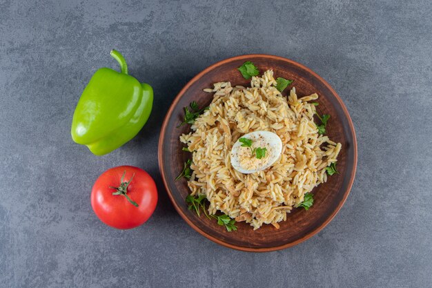 Rice with vermicelli on a plate next to vegetables on the blue surface