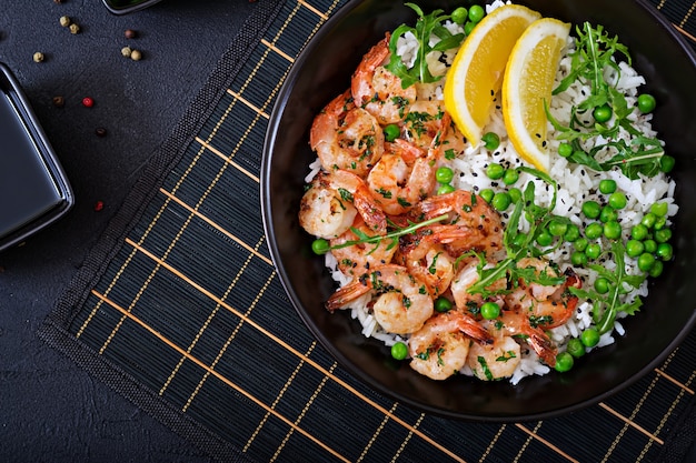 Rice with young green peas, shrimps and arugula in black bowl. Healthy food. Buddha bowl. Top view. Flat lay