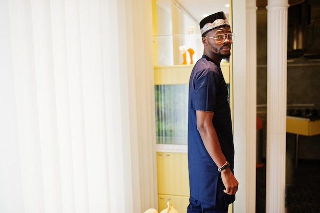 Rich african man in stylish traditional clothes and hat in glasses posed at room