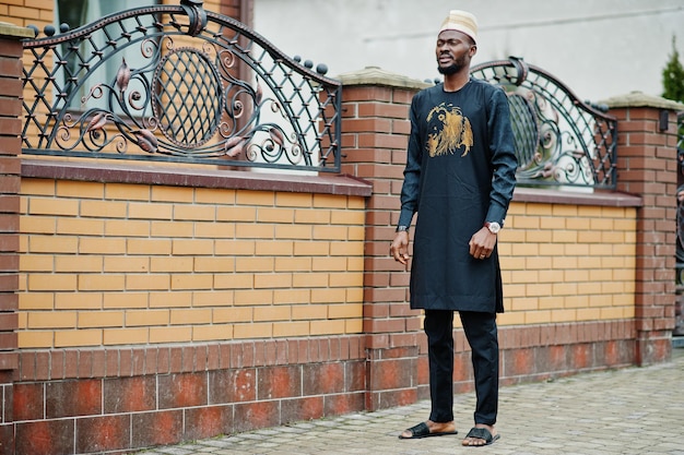 Rich african man in stylish traditional clothes and hat posed outdoor background his mansion