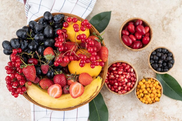 A rich assortment of fruits in bowls and a weaved basket on a towel on marble surface