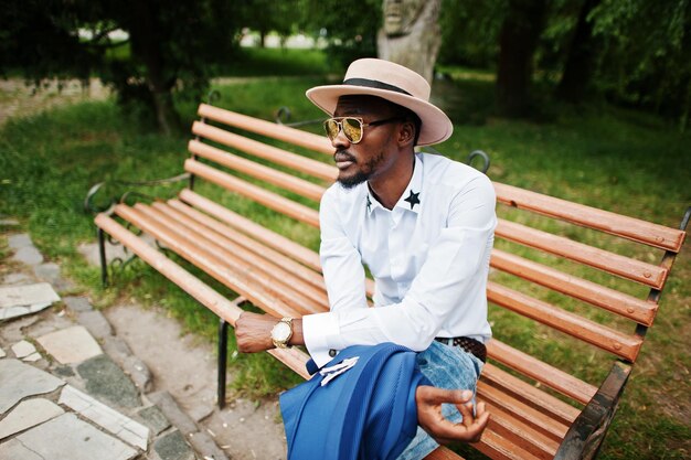 Rich black man sitting on bench at golden sunglasses and hat