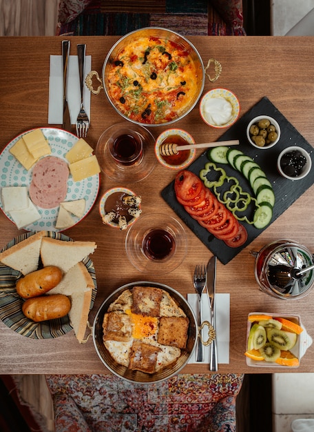 Rich breakfast table with wide selection of foods including eggs, sausages, cream cheese