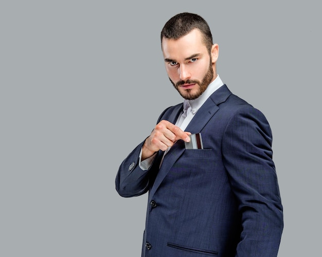 Rich male in a suit holding bank card. Isolated on grey background.