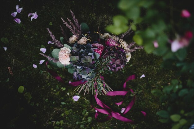 Rich wedding bouquet made of dark flowers and greenery lies on the green lawn