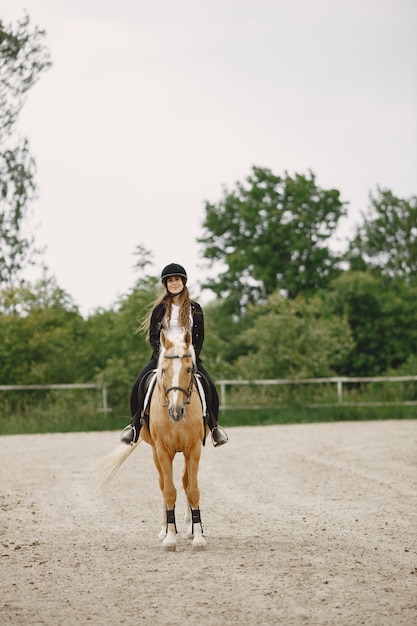 Женщина-всадник верхом на лошади на ранчо. У женщины длинные волосы и черная одежда. Женский наездник на своей коричневой лошади.