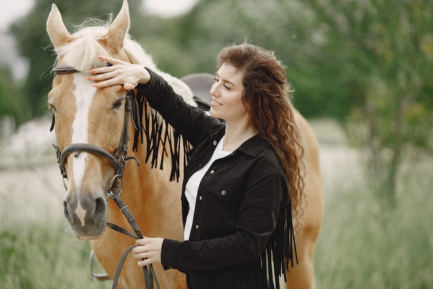 Donna del cavaliere che parla con il suo cavallo in un ranch. la donna ha i capelli lunghi e vestiti neri. equestre femminile che tocca le redini di un cavallo.