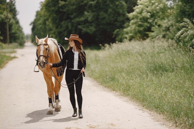道を馬と一緒に歩くライダーの女性。女性は長い髪と黒い服を着ています。馬の手綱を握っている女性の乗馬。