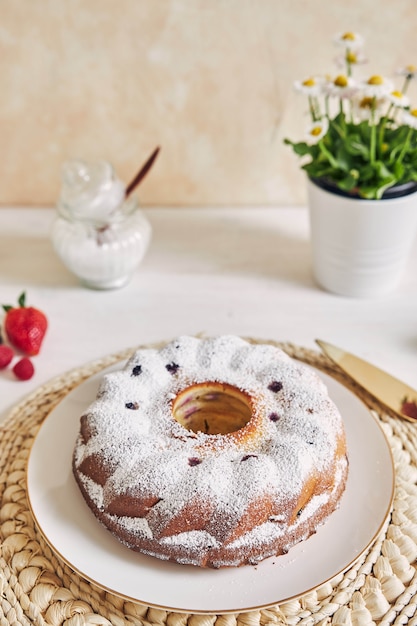 Ring cake with fruits and powder on a white table with white surface