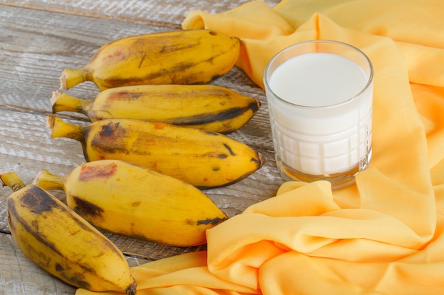 Ripe bananas with milk on wooden and textile, high angle view.