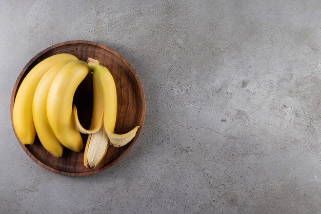 Ripe bananas on a wooden plate, on the marble surface
