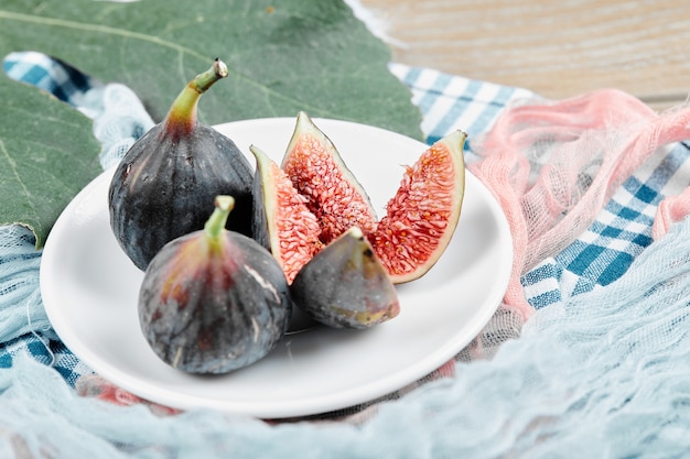 Free photo ripe black figs on white plate with a leaf and tablecloths.