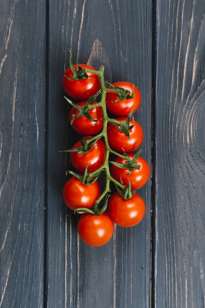 Ripe fresh cherry tomatoes on branch against black wooden plank