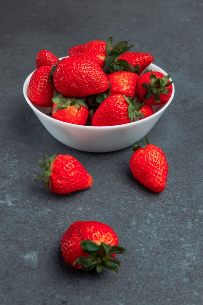 Ripe fresh strawberries in a white bowl side view on a grey grunge background