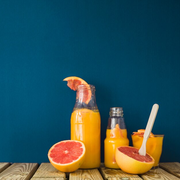 Ripe grapefruits with glass and bottles of juice on wooden table