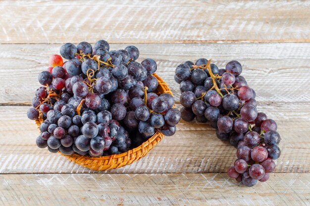 Ripe grapes in a wicker basket on wooden background, high angle view.