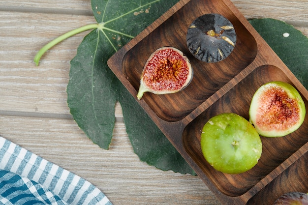 Спелый зеленый и черный инжир на деревянном блюде с листом и скатертью.
