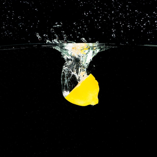 Ripe halved lemon falling into water splash against black background