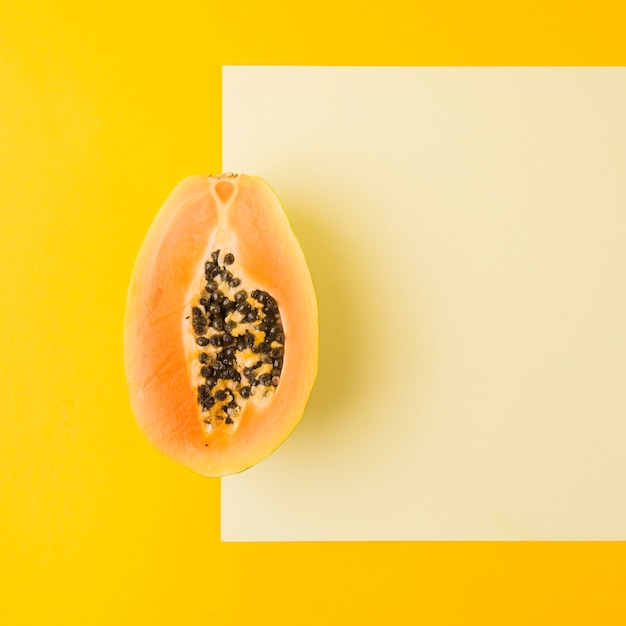 Ripe halved papaya on blank paper against yellow backdrop