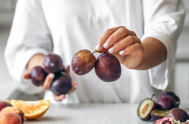 Free photo ripe homemade plums in the hands of a woman in the kitchen against the background of the kitchen table