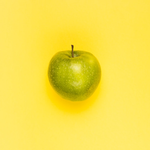 Спелое сочное зеленое яблоко на желтой поверхности