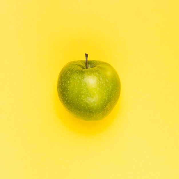 Ripe juicy green apple on yellow surface