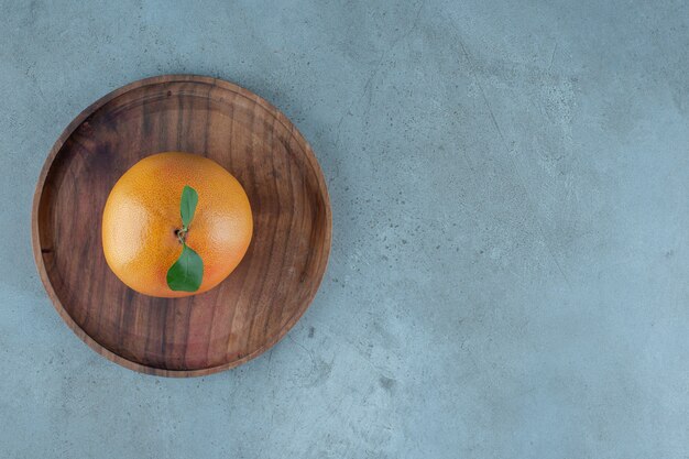 Спелый сочный апельсин на деревянной тарелке, на мраморном фоне. Фото высокого качества