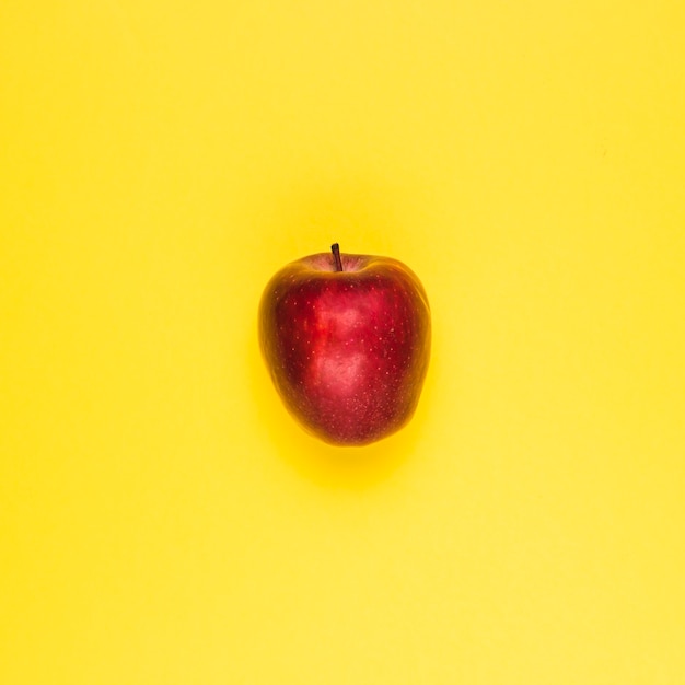 Ripe juicy red apple on yellow surface