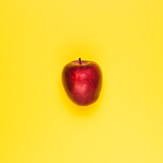 Ripe juicy red apple on yellow surface