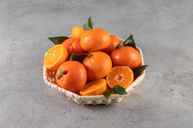 Ripe mandarins with leaves placed in wicker basket on stone surface