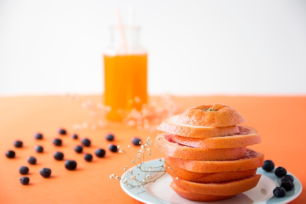 Ripe orange cut into slices with blueberries and gypsophila flower on an colored backdrop