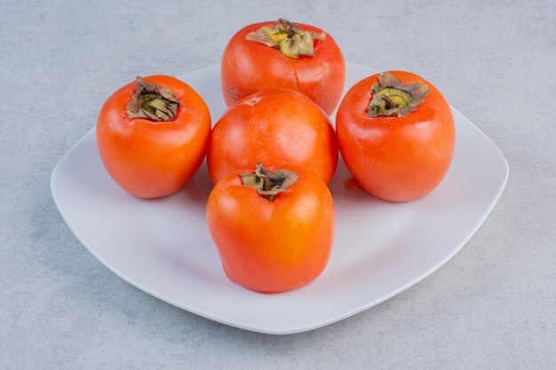 Ripe orange persimmon fruit on white plate. 