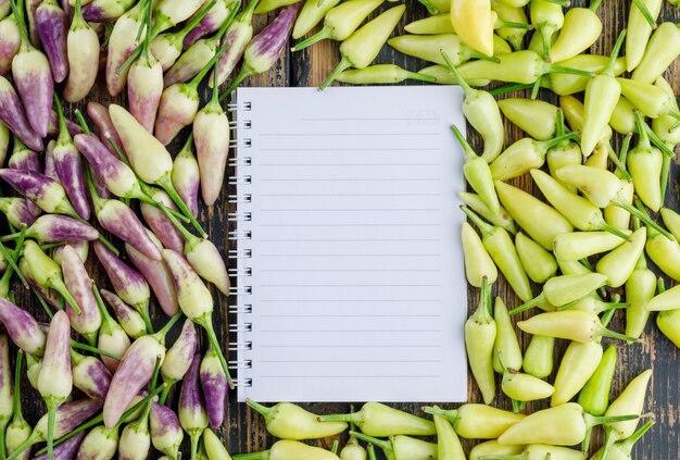 Ripe peppers with spiral notebook flat lay on a wooden