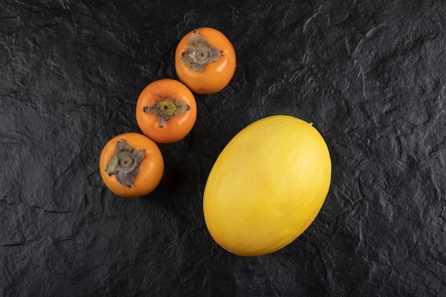 Бесплатное фото Спелые плоды хурмы и вкусная дыня на черной поверхности