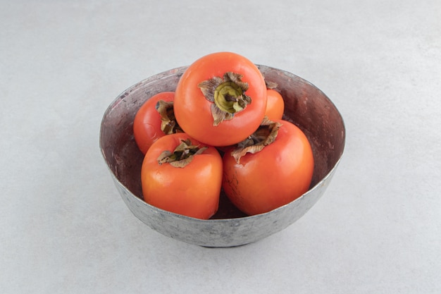 Ripe persimmon fruits in metal bowl.