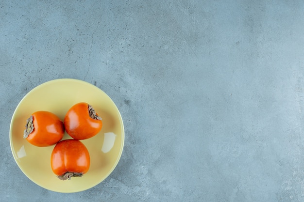 Ripe persimmon on a plate, on the marble background. High quality photo